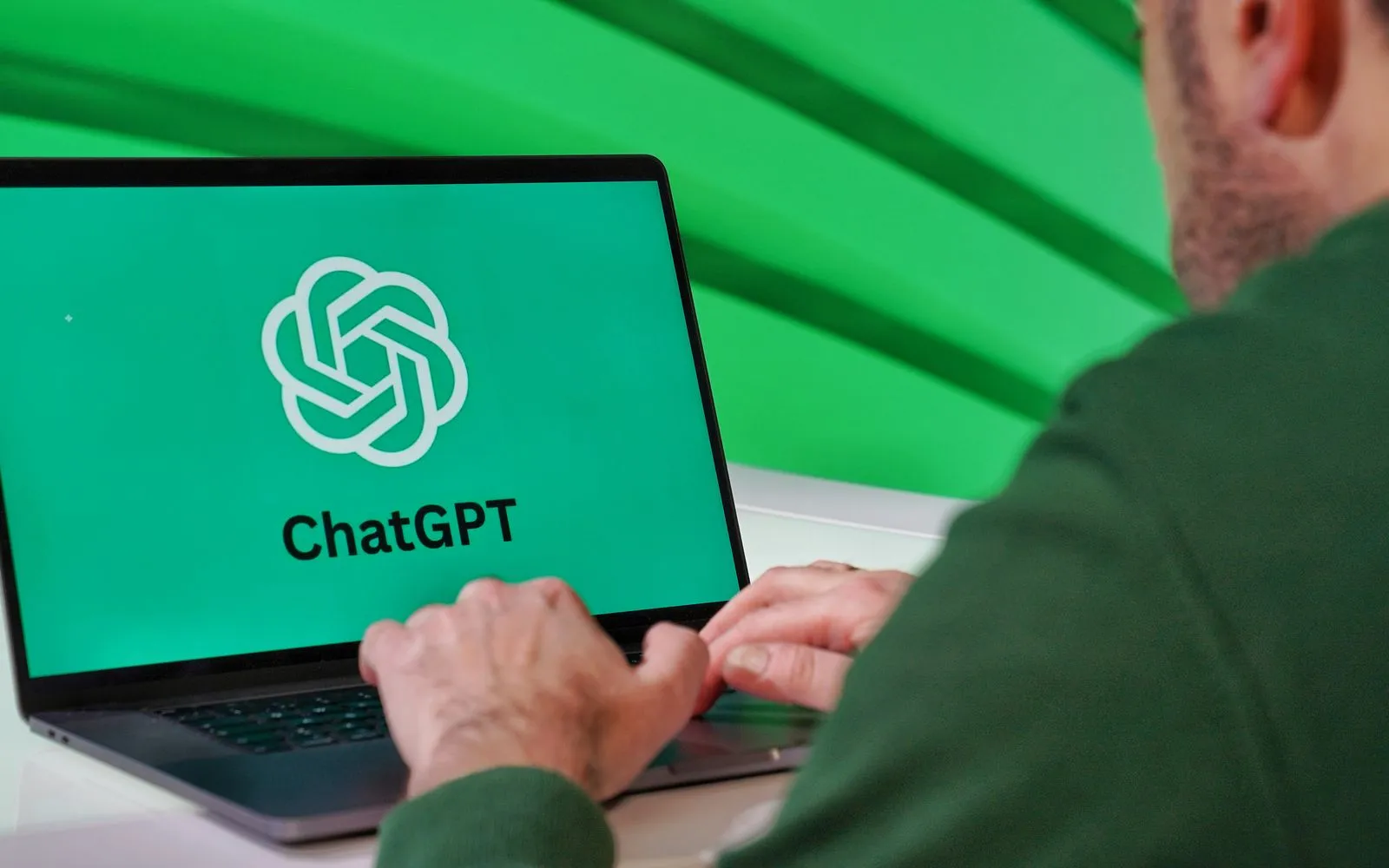 Person typing on a laptop displaying ChatGPT logo with a green vibrant setting.