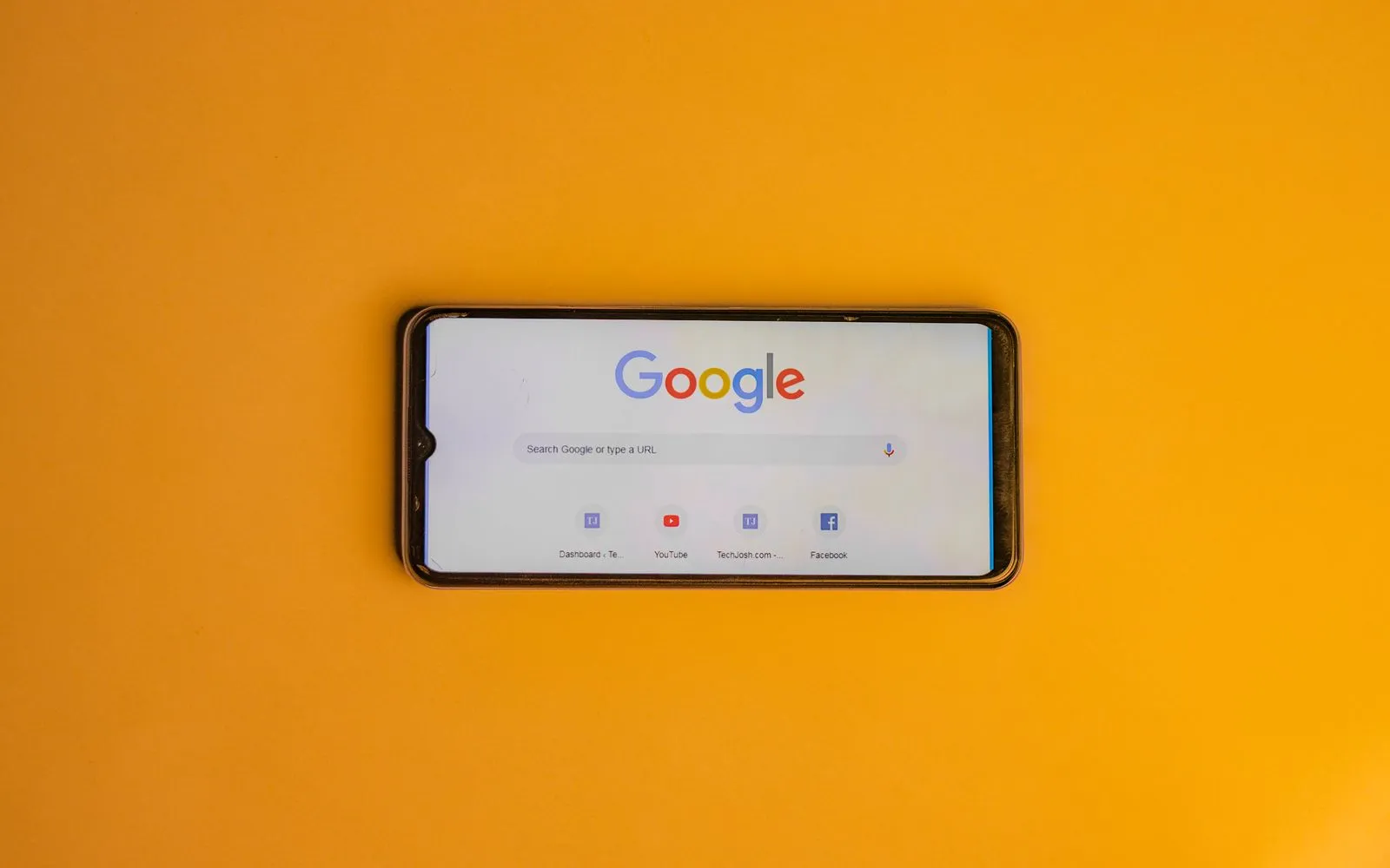 Smartphone displaying Google search page on a vibrant yellow background.