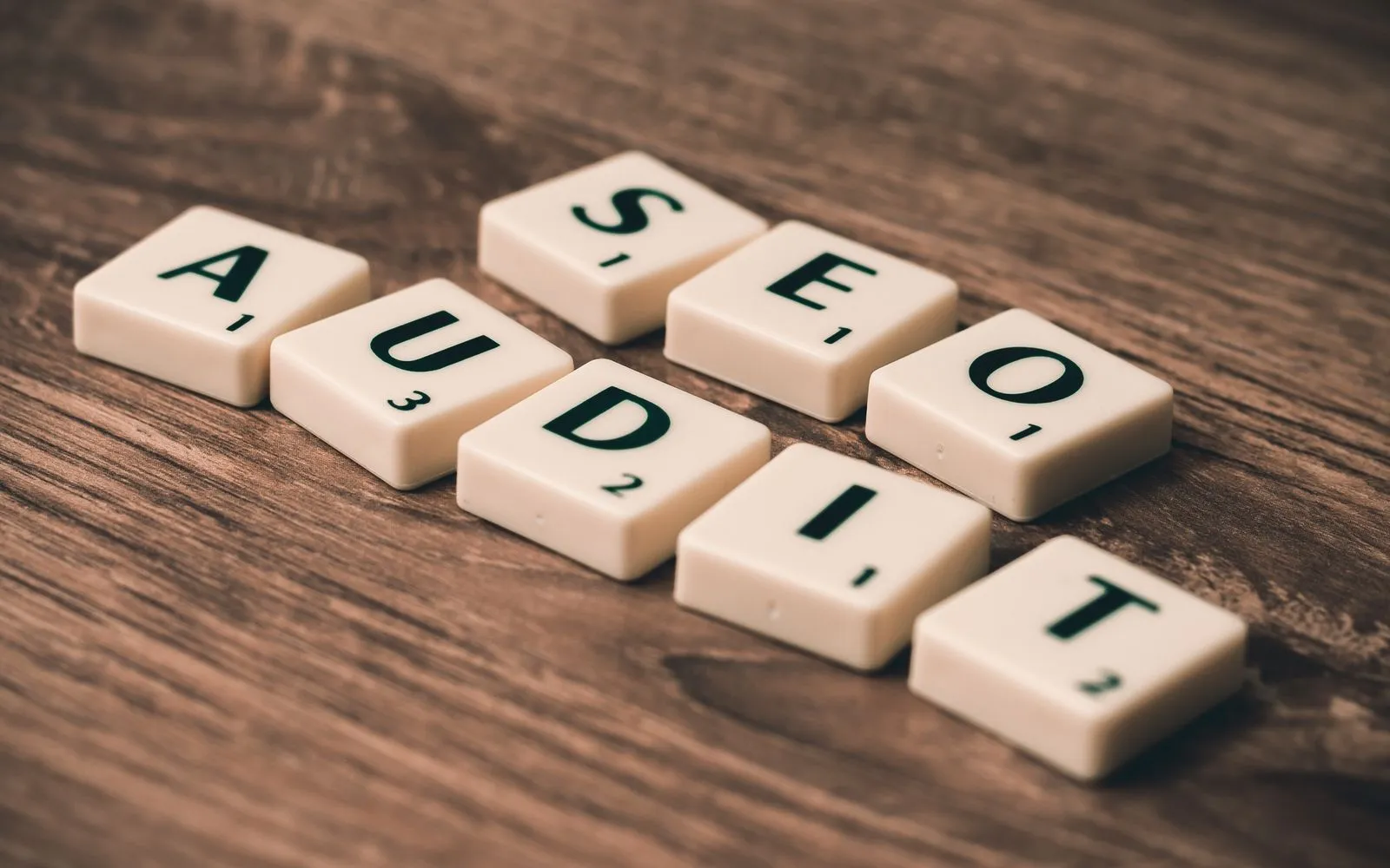 Scrabble tiles spelling SEO Audit on wooden surface, symbolizing digital marketing strategies.